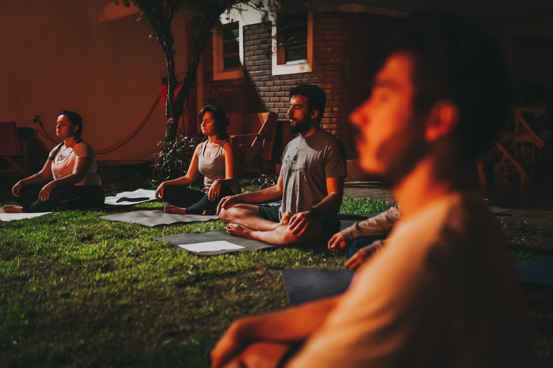 A group of people practicing yoga meditation outdoors at dusk in a peaceful garden setting.
